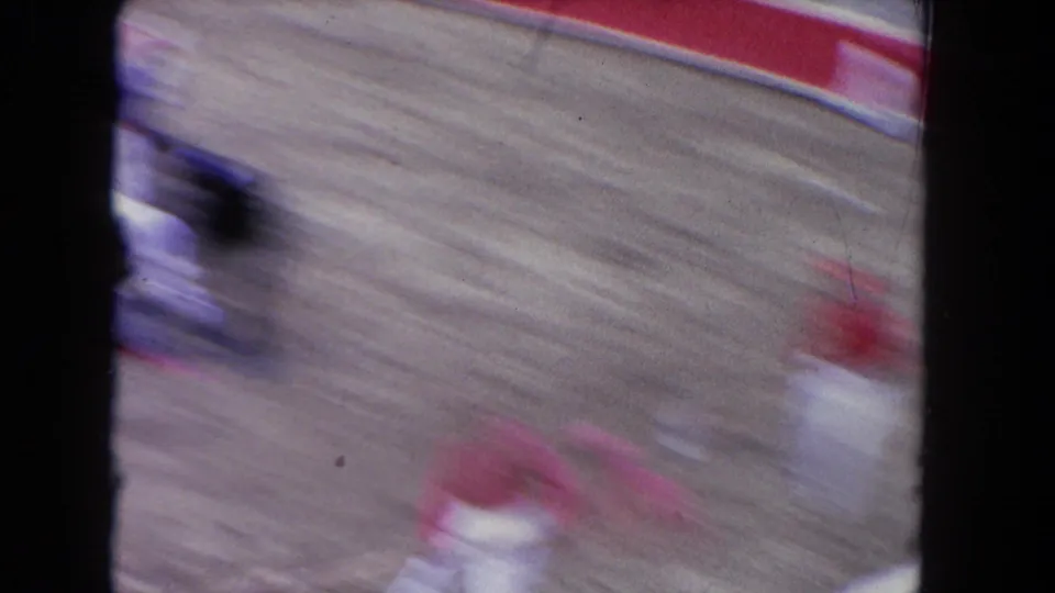 Motion-blurred 8mm frame from the Los Angeles arena scene, with a bullfighter and red cape crossing the sandy ring.
