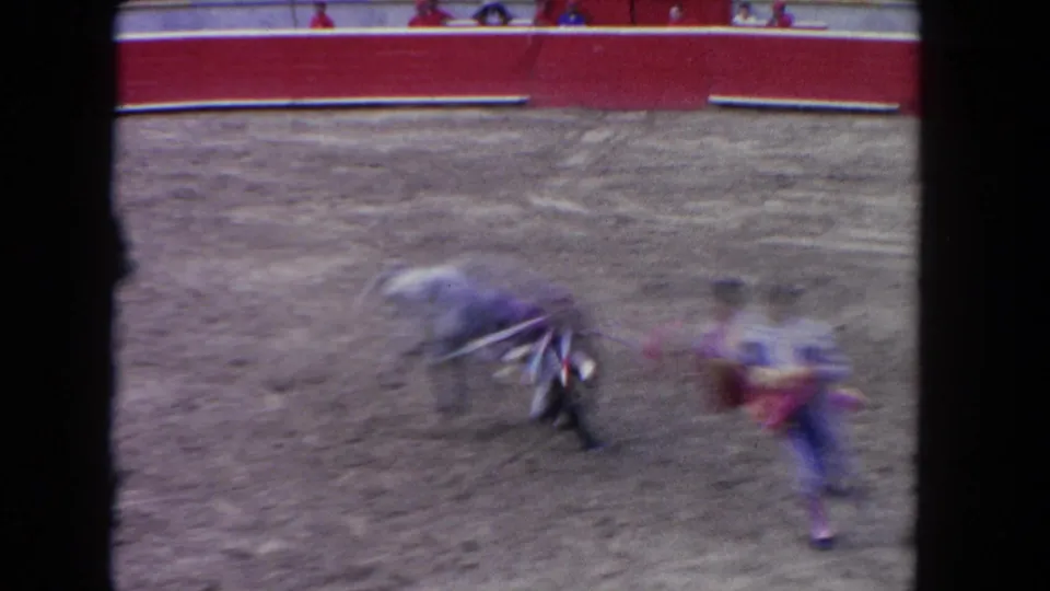 A motion-blurred 1962 Los Angeles home-movie frame captures the bull and matador moving fast across the arena.