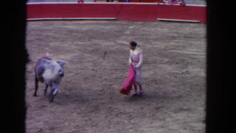 1962 Los Angeles 8mm frame showing a matador with red cape facing a gray bull across the dusty arena.