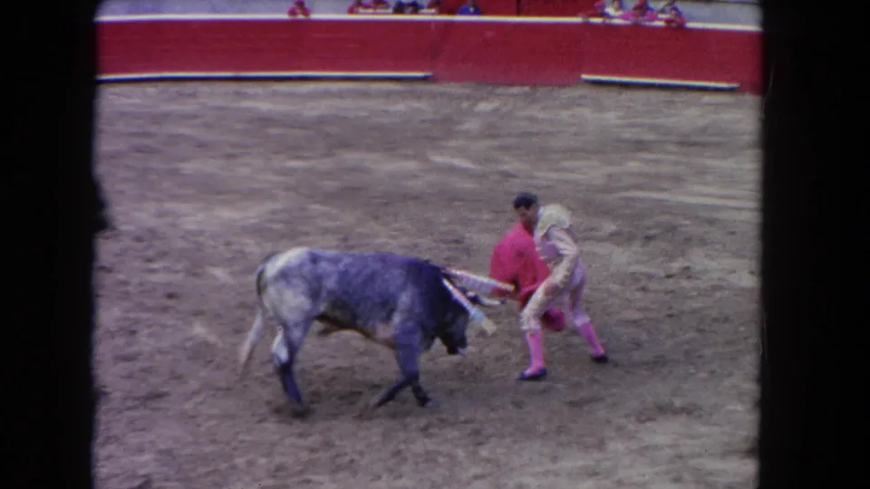 1962 Los Angeles home-movie frame of a gray bull passing close to a matador holding a red cape in the arena.