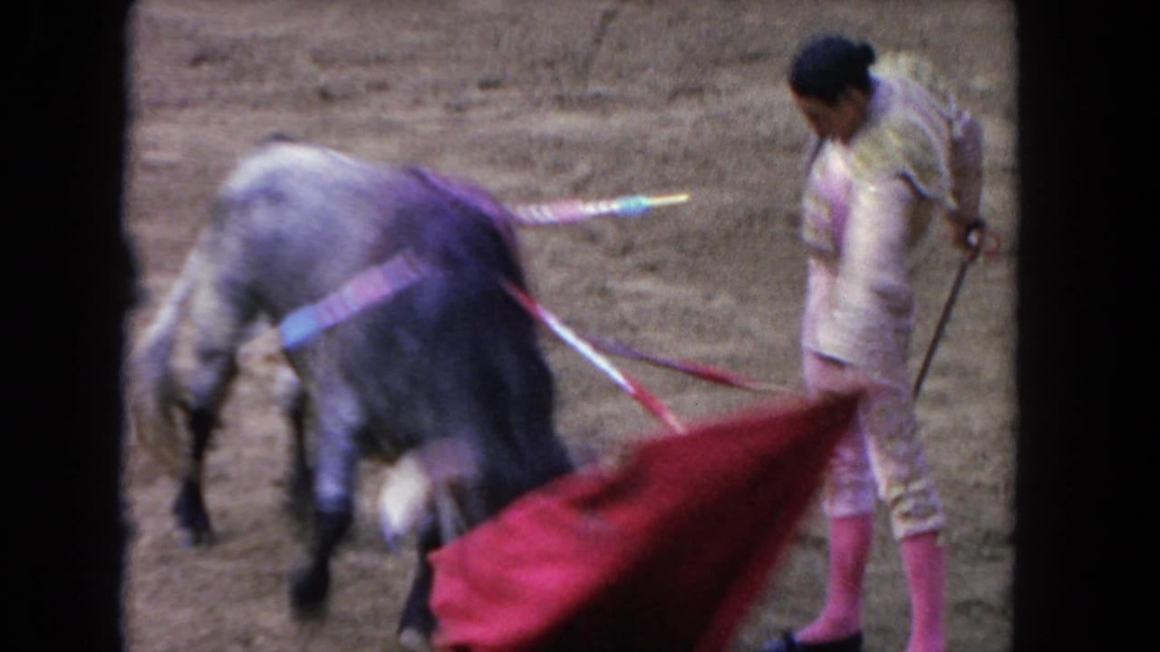 Matador swings a red cape near a bull in a sandy arena.