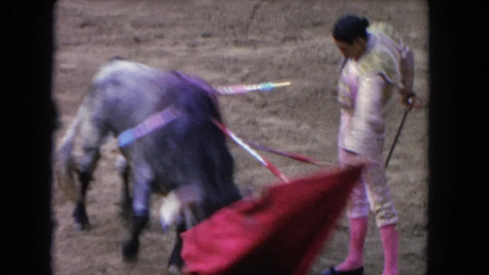 1962 Los Angeles 8mm frame showing a matador in a light suit drawing a bull past a red cape in a sandy bullring.