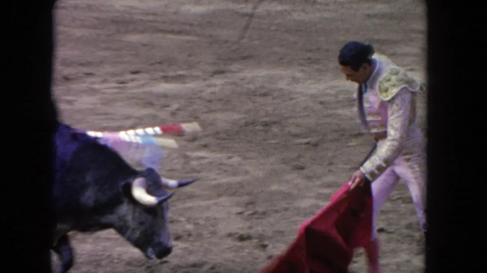 1962 Los Angeles 8mm frame showing the bull facing a matador who holds a red cape low in the sandy arena.
