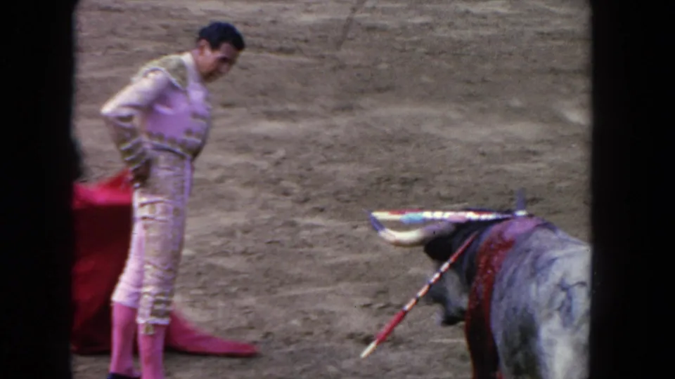1962 Los Angeles 8mm frame with the matador beside a red cloth and a decorated bull in the dusty ring.