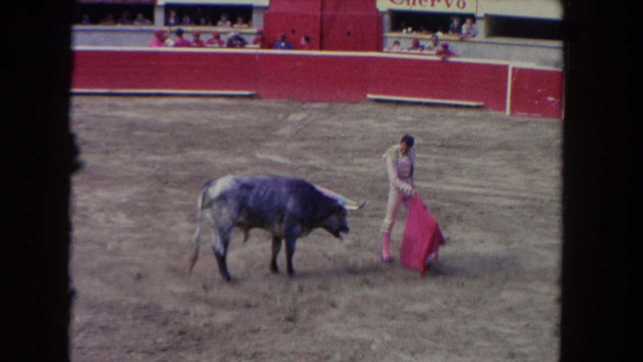 1962 Los Angeles 8mm frame showing a matador in pink and white attire facing a dark bull in a dusty red-walled arena.