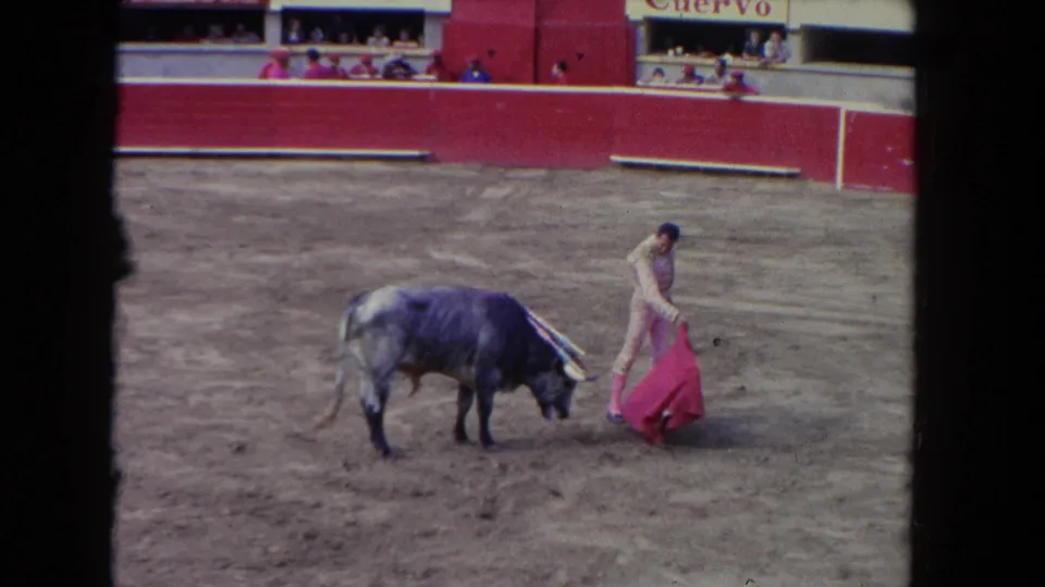 1962 Los Angeles bullfight frame showing a matador moving beside a grey bull with the red capote lowered near the sand.