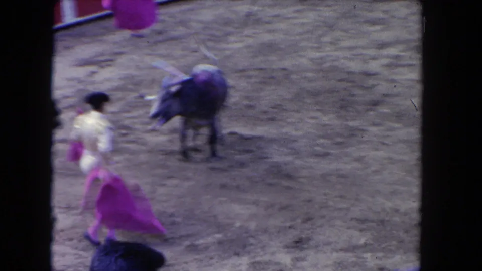 In 1962 Los Angeles footage, a matador in a light suit uses a purple cape while a bull approaches in a sandy arena.