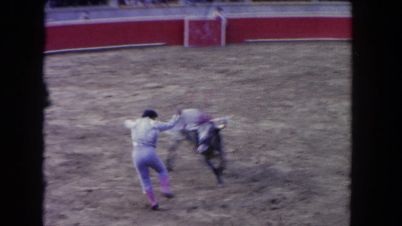 A matador in a light suit and black hat dodges a charging bull in a sandy Los Angeles arena, supported by 1962 metadata.