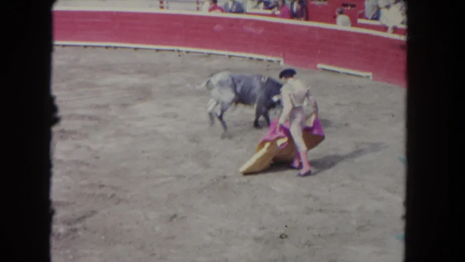 1962 Los Angeles 8mm frame with a matador beside a grey bull, holding a pink cape near a yellow cape in the arena.