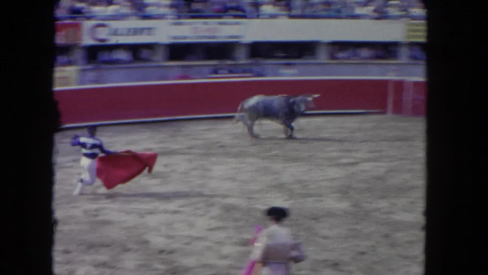 1962 Los Angeles 8mm frame showing a matador sweeping a red cape as the bull moves across the arena.