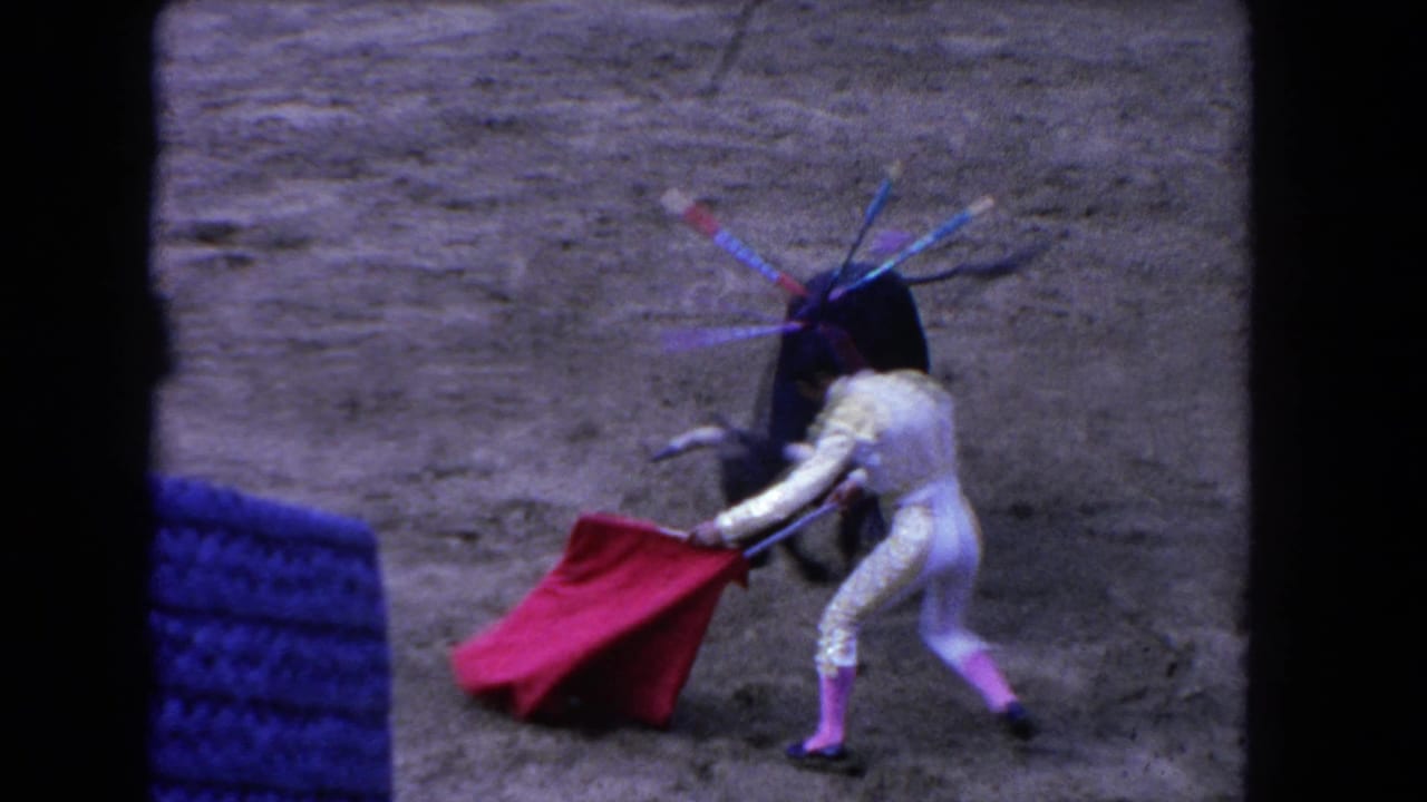 Matador with red cape faces a black bull on a sandy arena floor.