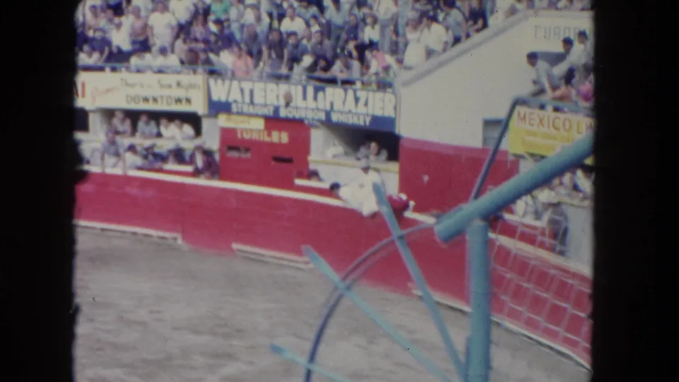 Los Angeles bullring frame showing a matador near the red wall, a bull in the arena, spectators, and visible concession signage.