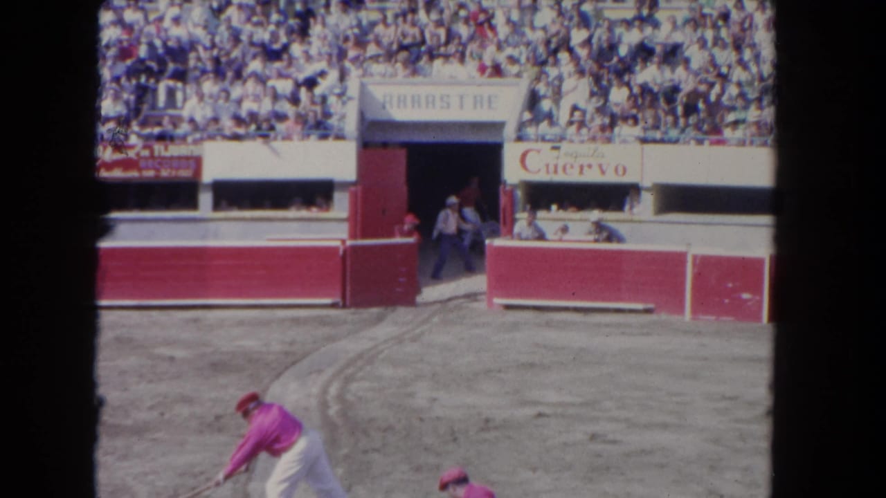 Visitor-shot 1962 Los Angeles arena frame showing the ARRASTRE entrance, crowd, Cuervo sign, and performers in pink and white.
