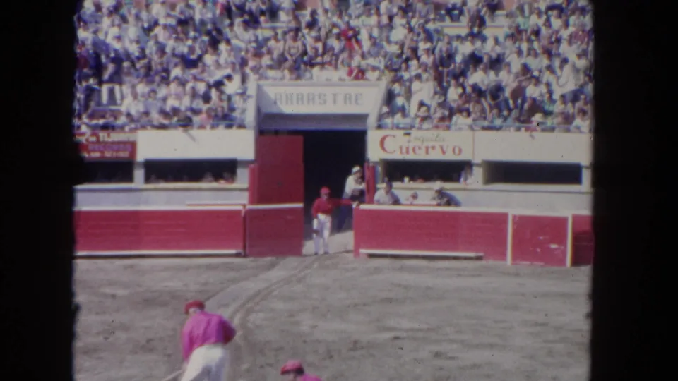 1962 Los Angeles bullfighting-style arena view with a performer in pink and white, spectators, tunnel doors, and visible advertising.