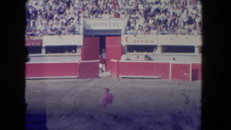 Faded 8mm frame from the 1962 Los Angeles arena clip, showing spectators, red-and-white barriers, signage, and a distant performer.