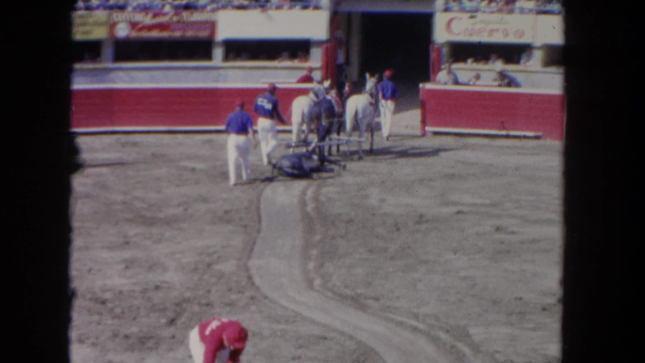 Several workers and horses gather near the barrier as a worker bends over the dirt track.
