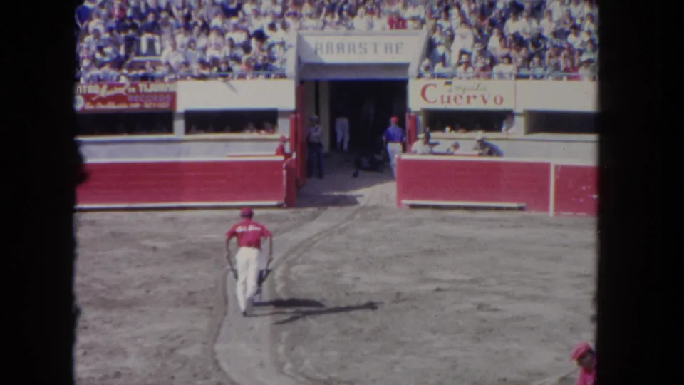 A worker in red walks along the prepared dirt path below crowded stands and visible racetrack advertising.