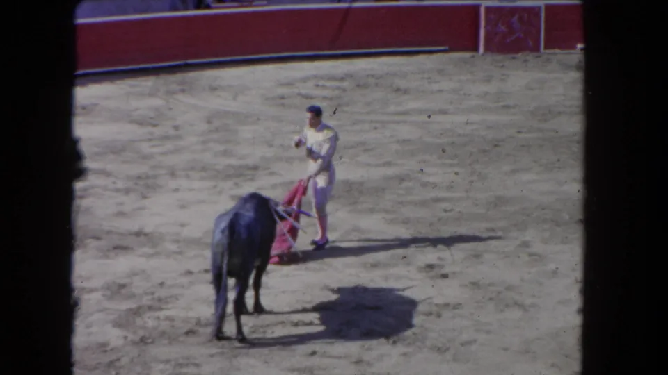 A bull stands near the bullfighter with the red cape lowered in a sandy Los Angeles arena scene dated by metadata to 1962.