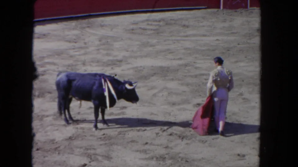 1962 Los Angeles 8mm frame showing a standoff between a decorated dark bull and a white-clad performer holding a red cape.