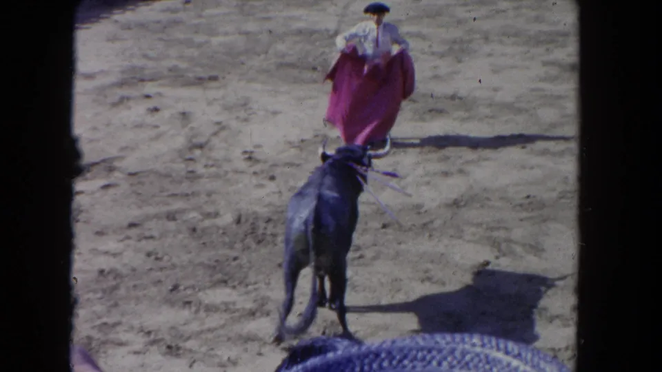 1962 Los Angeles 8mm frame looking over spectators toward a bull approaching a matador with an open cape.
