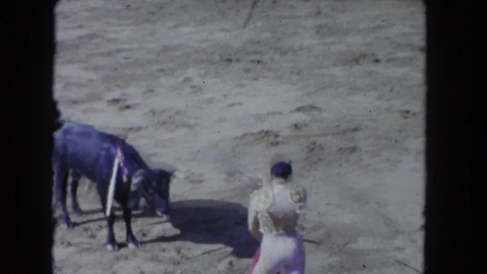 The performer stands with a red cape while the bull lowers its head on the sandy arena floor in the 1962 Los Angeles footage.
