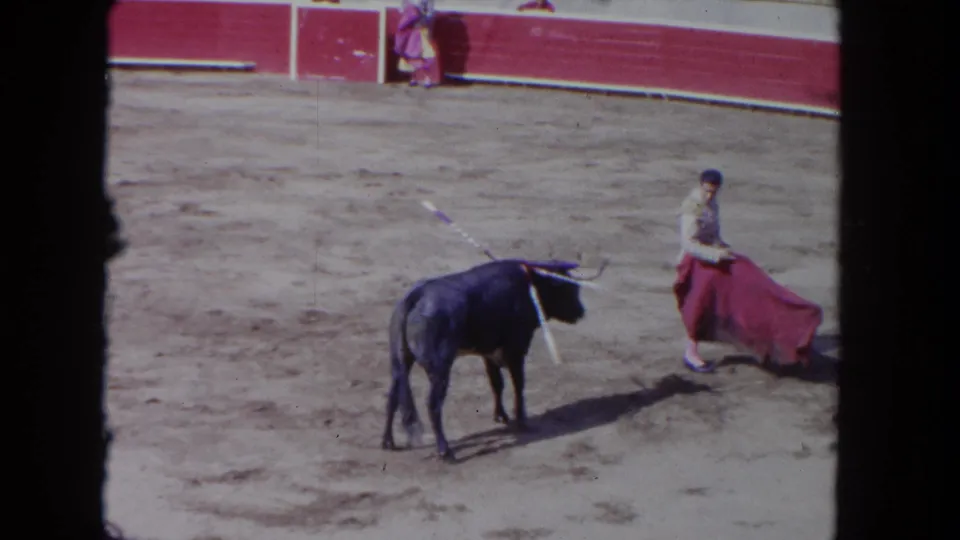 1962 Los Angeles 8mm frame with a dark bull bearing banderillas and a matador holding a red cape in the arena.