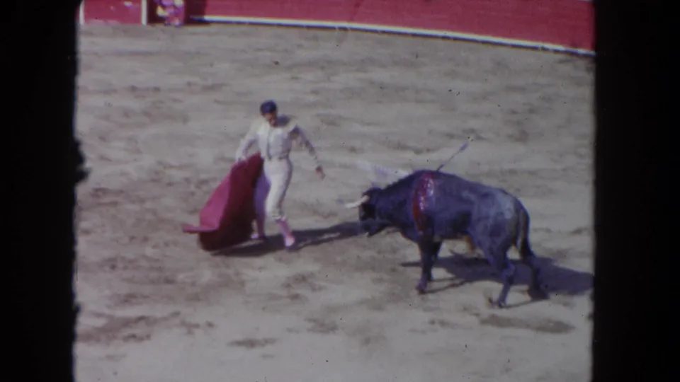 1962 Los Angeles 8mm frame showing the matador stepping with the red cape while the dark bull turns across the arena.