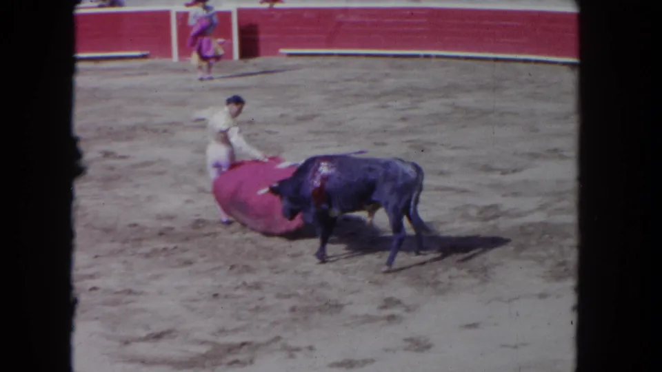 1962 Los Angeles 8mm frame showing the bull moving past the red cape during a matador-style pass in the sandy ring.