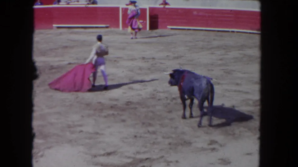 1962 Los Angeles 8mm frame with the matador-style performer turning away from a black bull in the sunlit arena.