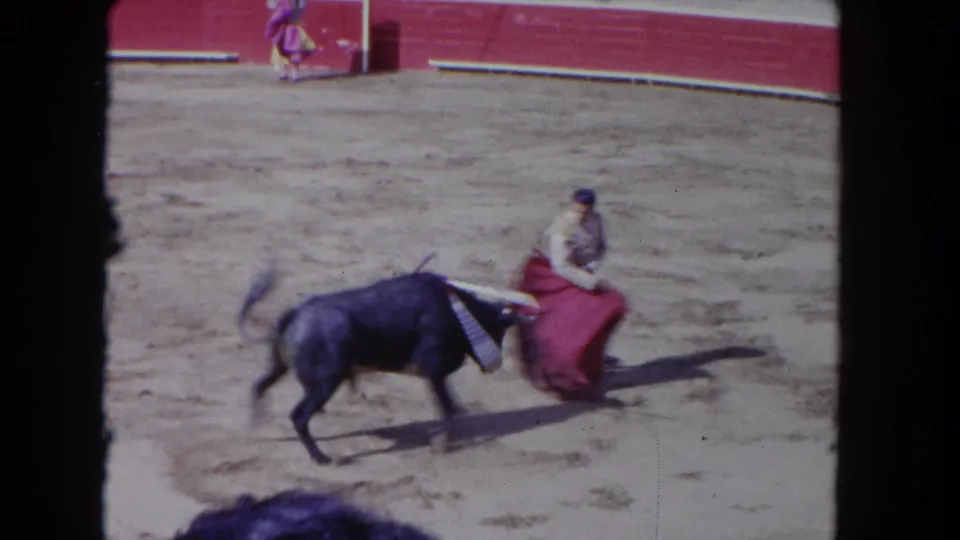 1962 Los Angeles 8mm frame showing a dark bull passing close to a matador-style performer low beside a red cape.