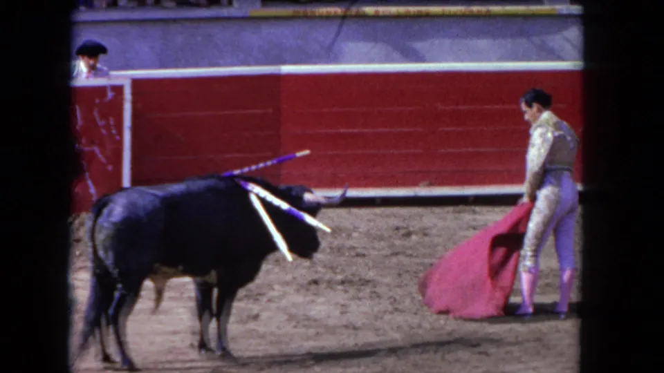 1962 Los Angeles 8mm frame showing a matador and red cape opposite a black bull with banderillas in a sandy arena.