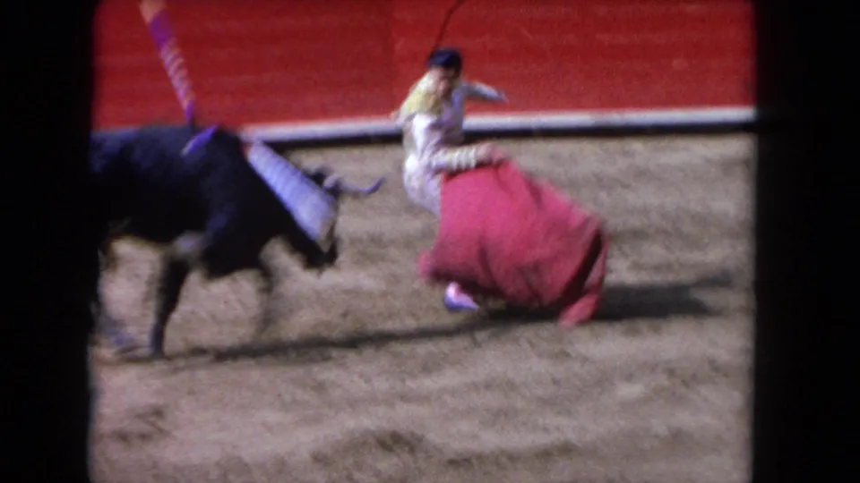 The matador pivots with the red cape as the charging black bull passes close by in the 1962 arena footage.