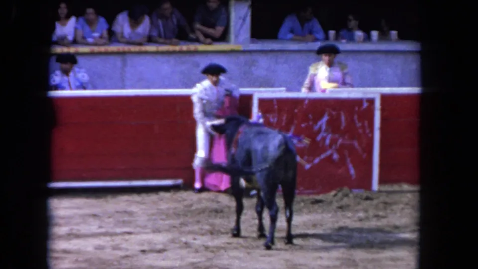 A matador-style performer stands near the bull and barrier, with spectators visible above, in the 1962 Los Angeles 8mm clip.