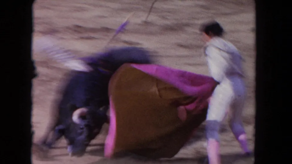 1962 Los Angeles 8mm frame showing a matador in a light suit using a pink cape as a black bull charges past.