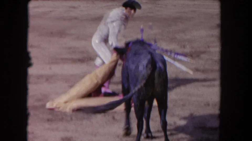 1962 Los Angeles 8mm frame showing the matador close behind the bull, with tan and pink cape fabric on the sandy ground.