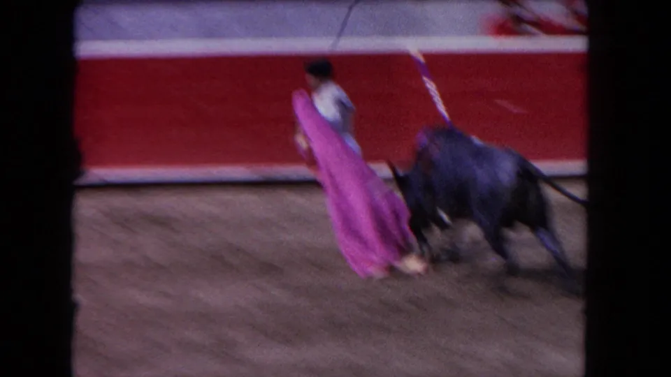 1962 Los Angeles frame showing a matador and black bull in motion near a red arena barrier during a cape pass.