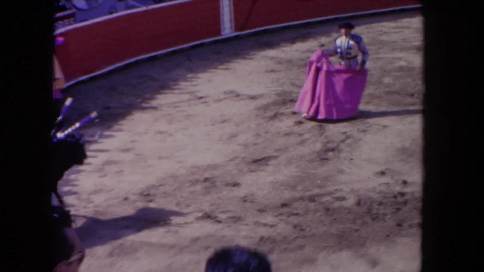 1962 Los Angeles 8mm frame showing a matador with a pink cape facing a bull near the edge of a sandy arena.