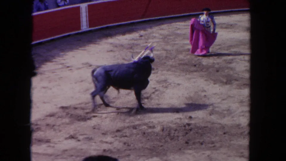 1962 Los Angeles 8mm frame showing the bull paused or turning toward a matador with a pink cape in the arena.
