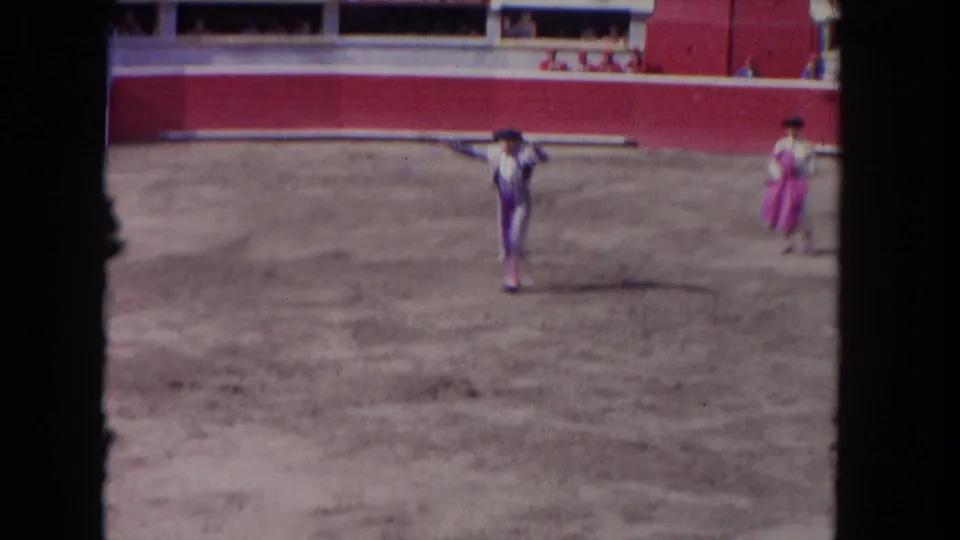 1962 Los Angeles home-movie frame showing a matador in a sandy bullfighting arena with another costumed participant nearby.