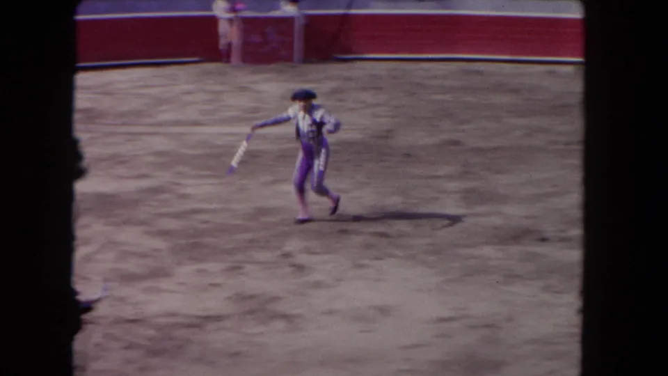 Matador in a striped suit and black hat crosses the sandy arena during the Los Angeles bullfighting event.