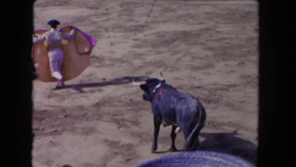 8mm frame showing the matador carrying the cape away as the black bull watches from the lower right of the arena.