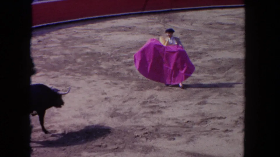 The torero steps across the sandy Los Angeles arena with a purple cape while the bull appears at the edge of the frame.