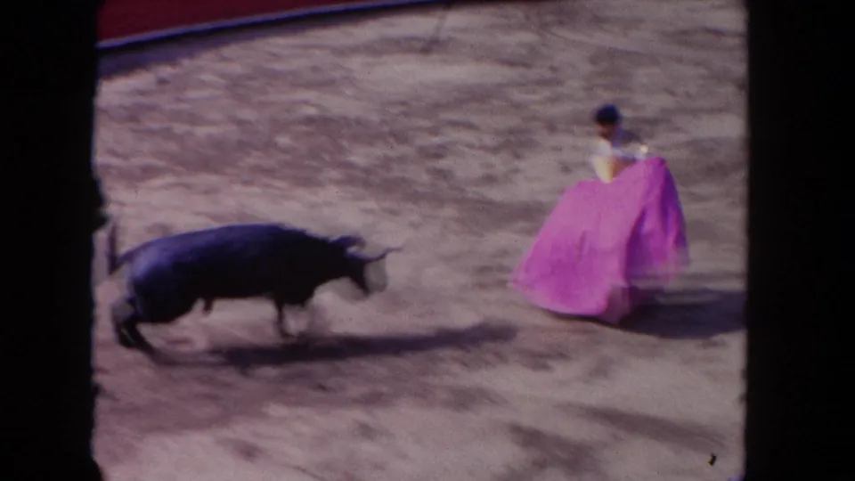 A blurred 8mm frame captures the bull charging past the torero and purple cape in the Los Angeles bullfight arena.