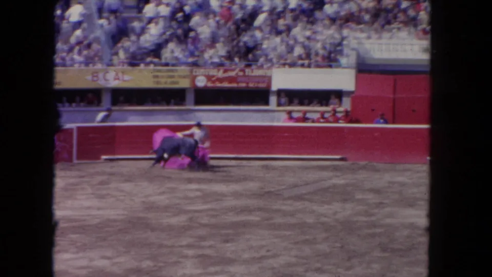 1962 Los Angeles 8mm frame showing a matador using a pink cape as a black bull charges in a dirt arena.