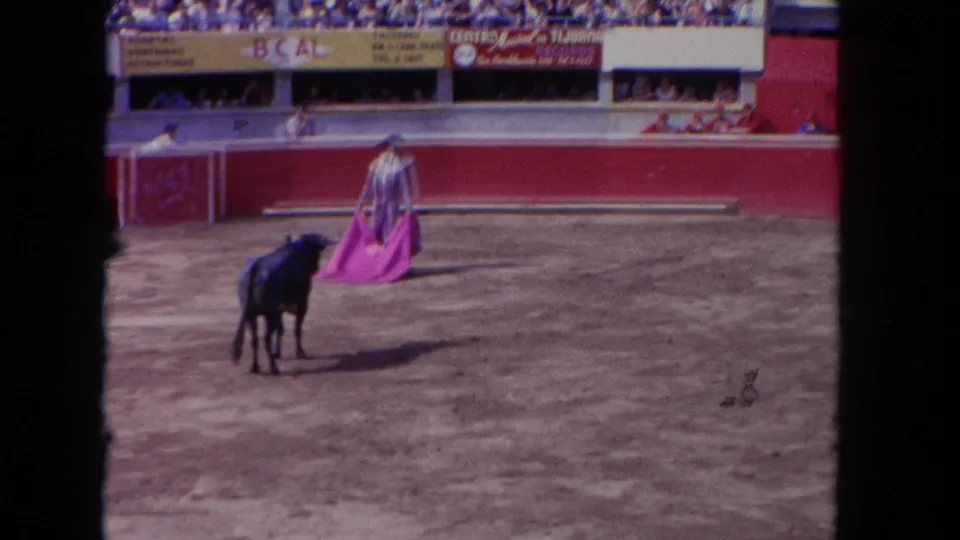 1962 Los Angeles 8mm frame of a black bull facing a matador draped in a pink cape inside the dirt ring.