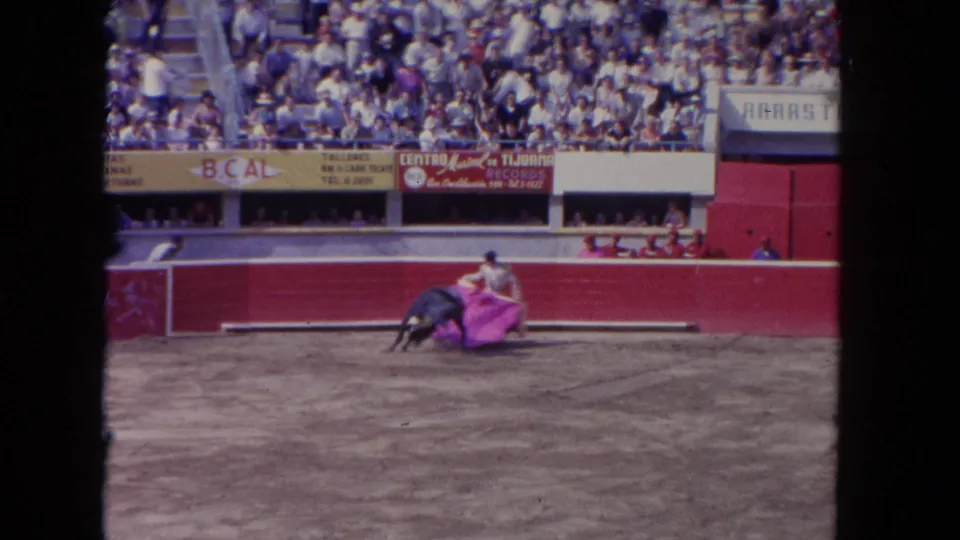 1962 Los Angeles 8mm frame showing a matador sweeping a pink cape as a dark bull passes in the sandy ring.