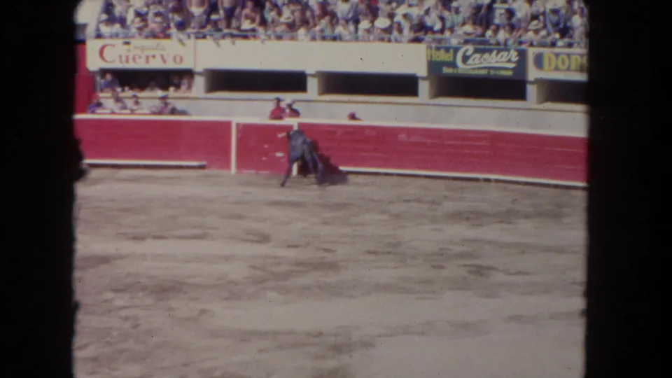 1962 Los Angeles 8mm frame showing the black bull near a matador or handler with a purple cape at the red arena barrier.