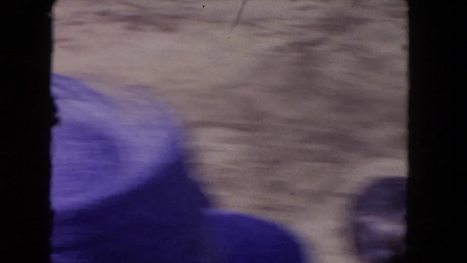 Soft 8mm frame from the 1962 Los Angeles arena clip, showing sandy ground, foreground spectators, and heavy black film-frame edges.