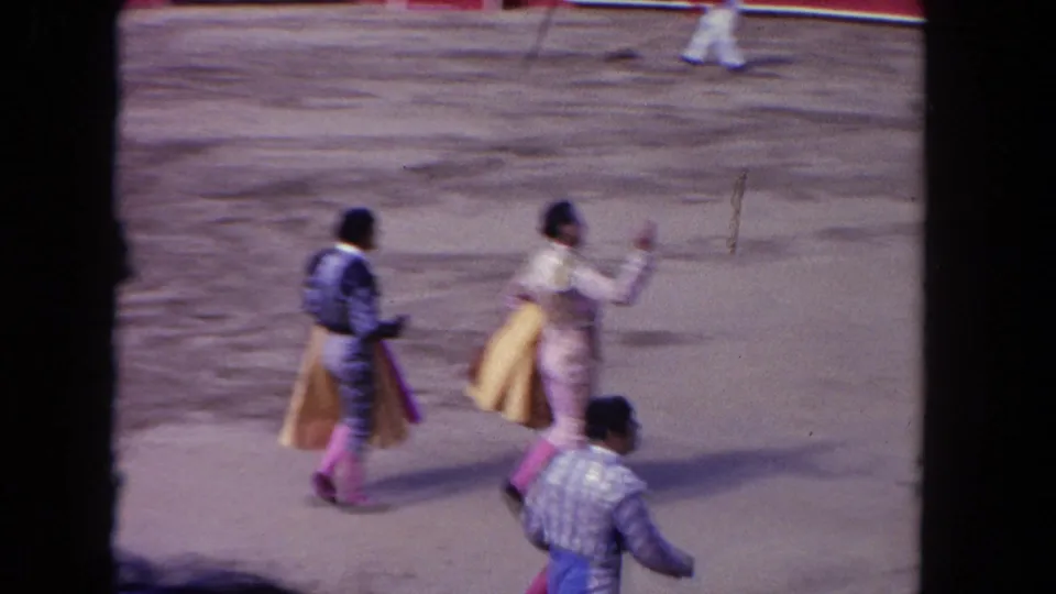 1962 Los Angeles frame with matadors in formal bullfighting attire crossing the ring, one holding a cape and another gesturing ahead.
