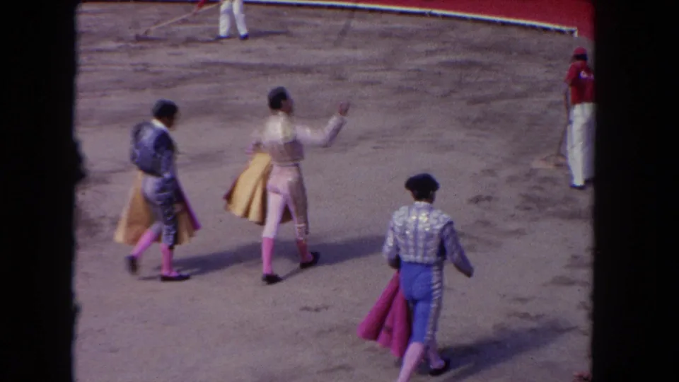 Matadors in 1962 Los Angeles arena footage walk across the ring, one raising a hand while another trails with a red cape.